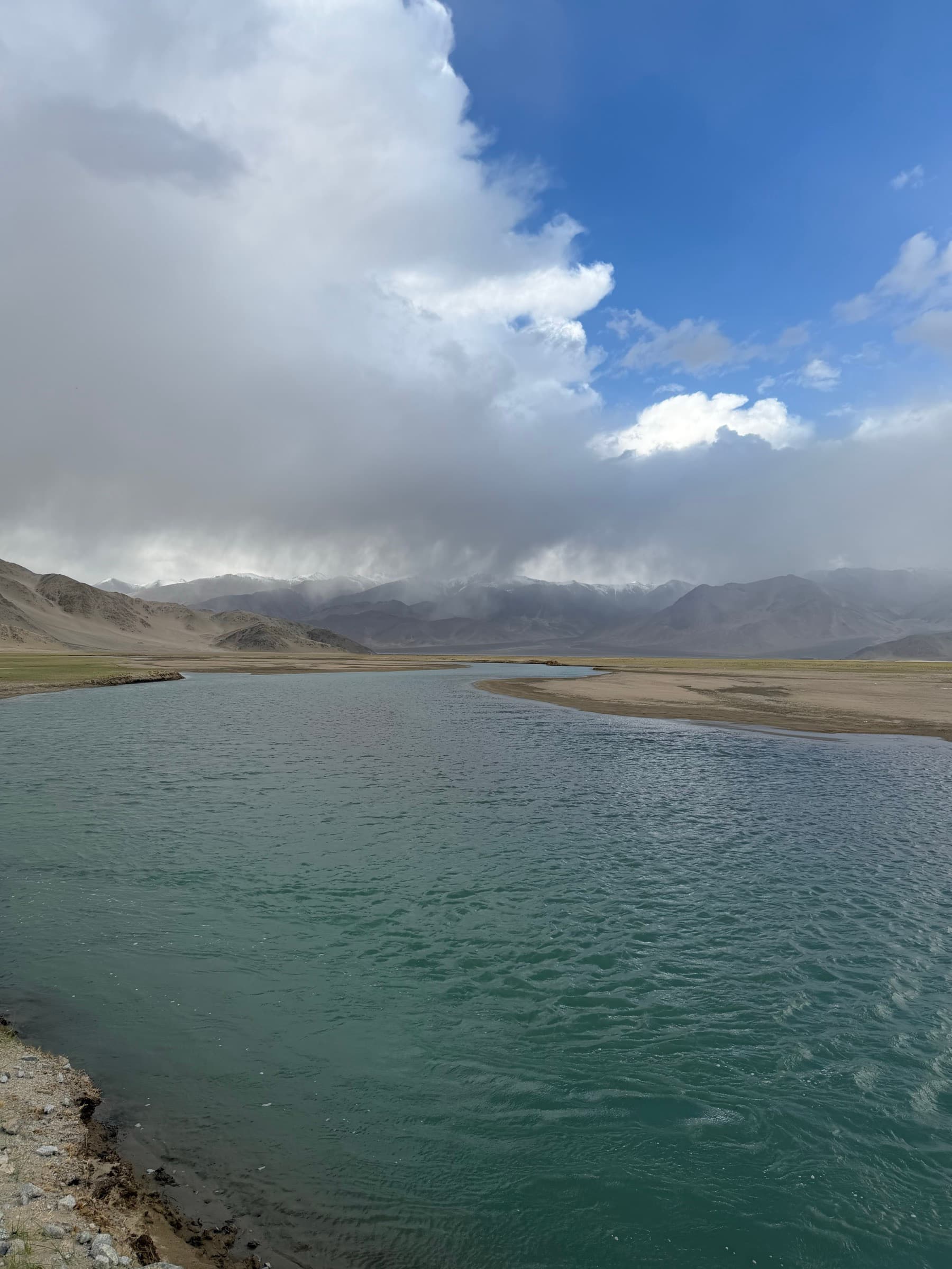 A turquoise river beneath storm clouds and distant mountains