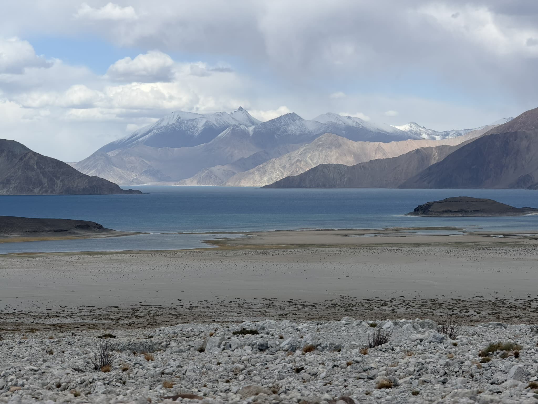 A blue lake below a range of snow-capped mountains