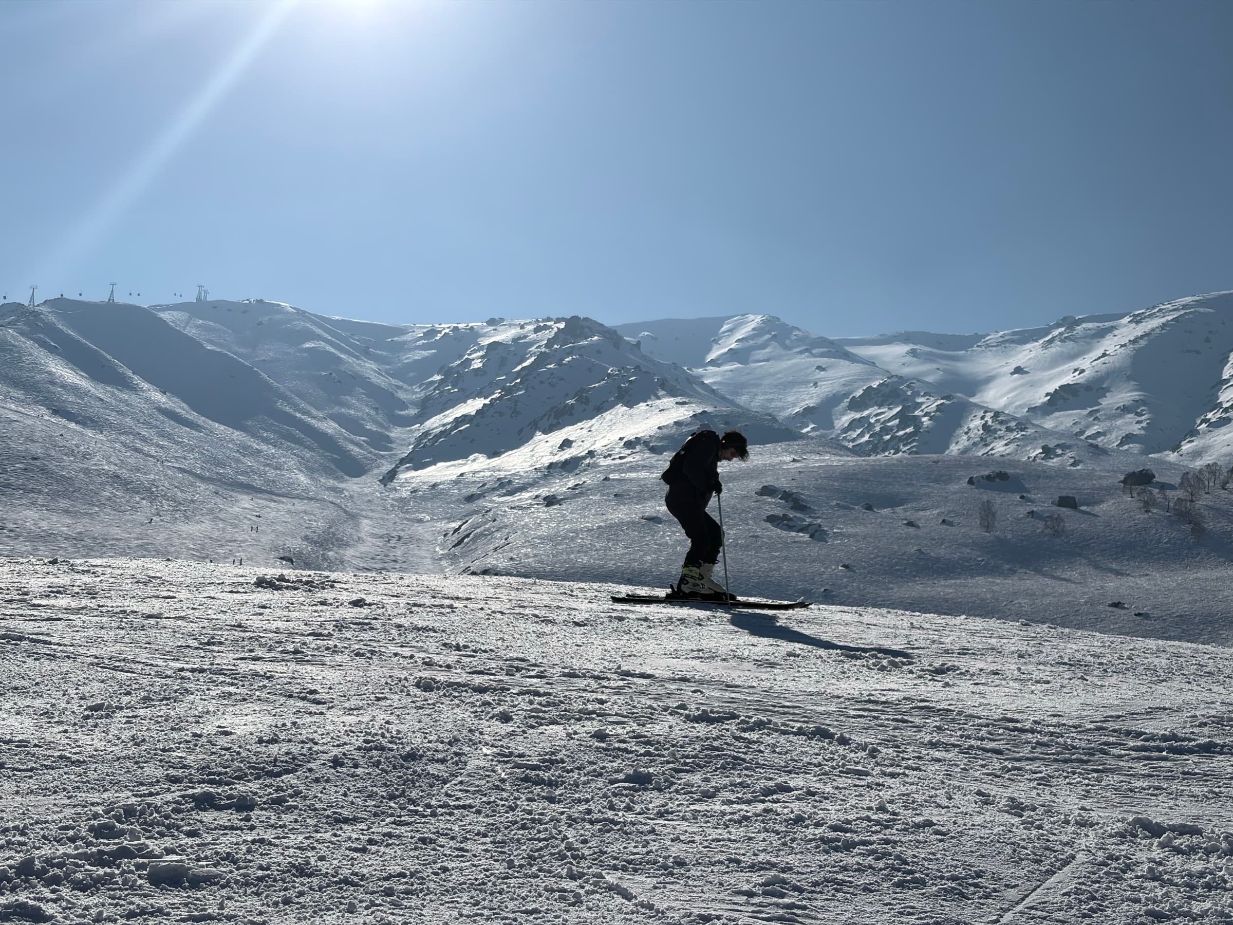 A skier crossing a sunlit slope beneath snowy mountains